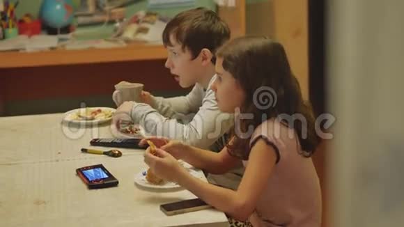 男孩和女孩的家庭生活方式孩子们在餐桌上吃饭喝茶吃蛋糕看电视视频的预览图