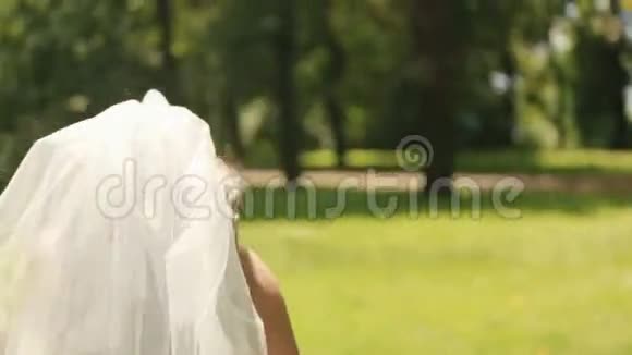 美丽的美丽的新娘穿着华丽的白色连衣裙带着长长的面纱在公园的草坪上嬉戏地跑掉了视频的预览图