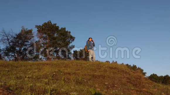 女孩旅行者站在山顶喝咖啡的玻璃杯旅游妇女喝热茶看日落视频的预览图