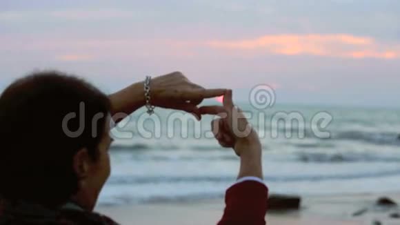 在海滩上日落时分女人用双手描绘太阳视频的预览图