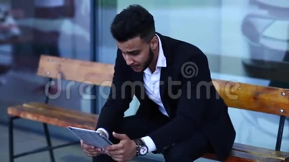 穿着阿拉伯服装的男人在商务中心附近无聊地使用平板电脑视频的预览图