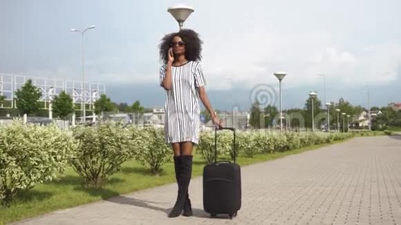 带着行李的带墨镜的优雅微笑的非裔美国商务女士在机场的完整视野视频的预览图
