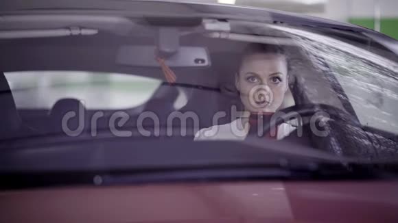 漂亮的女人穿着白色衬衫坐在方向盘后面的红色汽车上视频的预览图