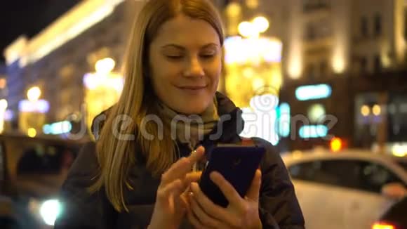 美丽迷人的年轻女人站在街上用她的智能手机城市灯光视频的预览图
