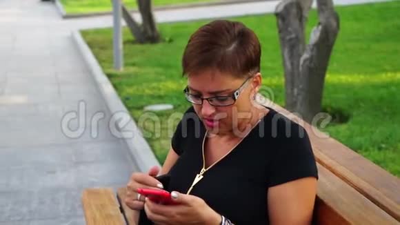 戴眼镜的年轻女子在一个城市公园里用手机聊天视频的预览图