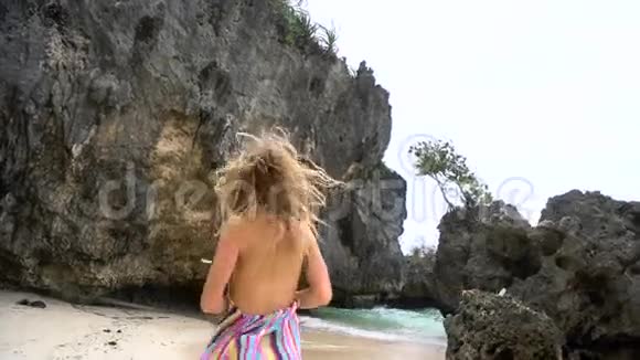 年轻的金发女孩穿着一件鲜艳的连衣裙沿着白色的海滩奔跑微笑着看着相机长出了头发视频的预览图