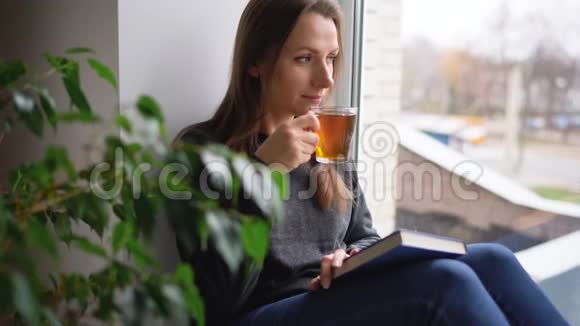 一位美丽的年轻女子坐在窗台上喝茶看书视频的预览图