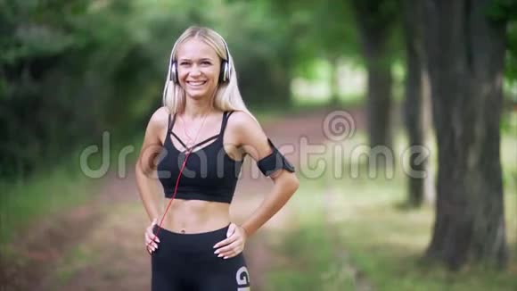 一个戴着耳机在公园微笑的女人的肖像视频的预览图