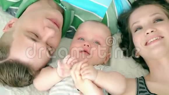 家庭幸福妈妈爸爸和六个月大的宝宝一家人躺在床上看着摄像机微笑着视频的预览图