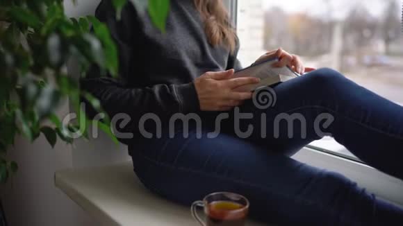 一位美丽的年轻女子坐在窗台上喝茶看书视频的预览图