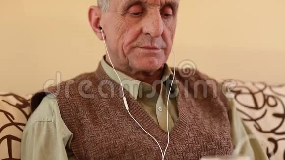 戴着白色智能手机的老人坐在沙发上听音乐视频的预览图