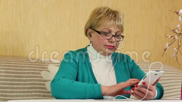 一位年长的女士坐在女偶上使用白色手机视频的预览图