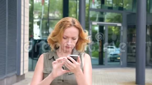 带电话的女孩在一个炎热的晴天在一个现代城市散步摩天大楼的背景4k慢动作视频的预览图