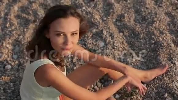 微笑的女孩坐在沙滩卵石上视频的预览图