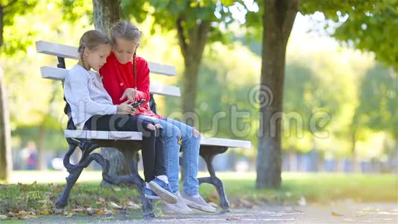 秋天带智能手机的可爱小女孩孩子们在温暖阳光的秋日户外玩耍视频的预览图