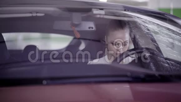 穿着白色衬衫的漂亮女性坐在方向盘后面的红色汽车上视频的预览图