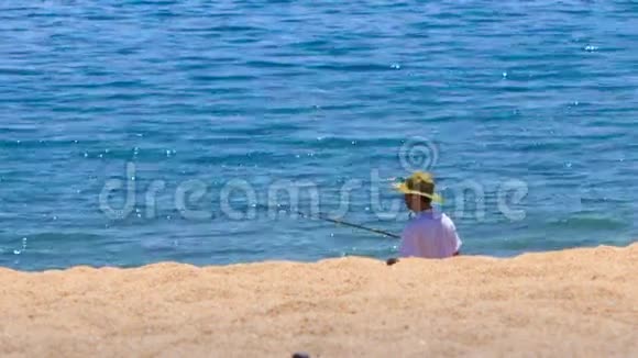 渔人戴着帽子用鱼竿在沙滩上拍打蔚蓝的大海视频的预览图