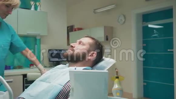 女牙医坐下来检查男性病人的牙齿投中弹视频的预览图