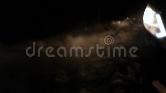 冬天的夜晚雪和烟在机器前灯的灯光下旋转慢动作视频的预览图