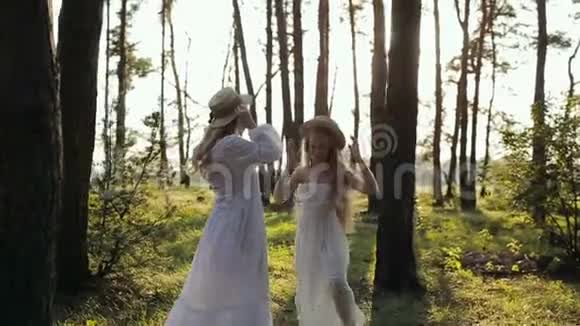 日落时分母亲和女儿穿着白色连衣裙戴着草帽在树林里玩耍视频的预览图