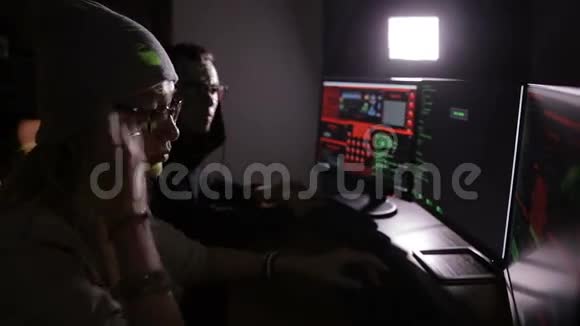 在黑暗的房间里在显示屏幕上使用数据代码的计算机上工作的男性和女性黑客视频的预览图
