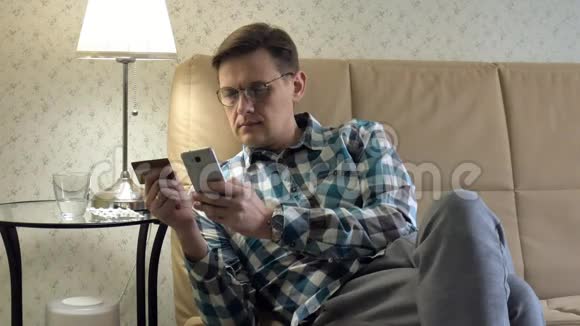 一个在网上买东西的人用手机和信用卡在沙发上家庭购物手机客户特写手持手机视频的预览图