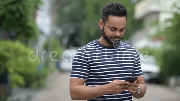 年轻的留胡子的印度男人在户外打电话视频的预览图