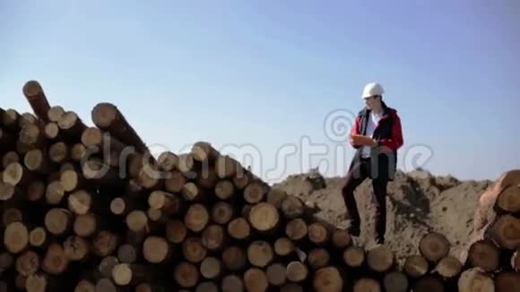 一个戴着白色头盔和红色夹克的建筑工人站在一堆原木上视频的预览图
