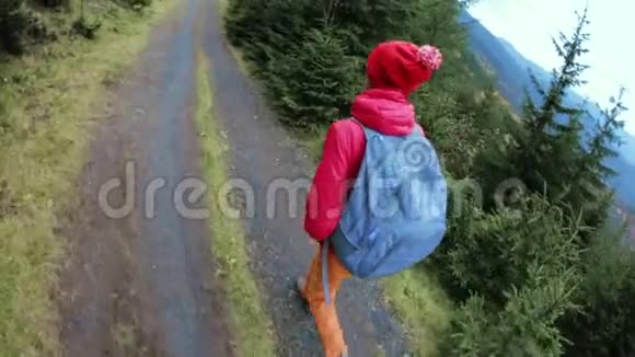 女徒步旅行者带着背包穿着红色夹克和橙色裤子走在山上的背景上视频的预览图
