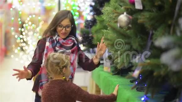 母亲和孩子在超市选择圣诞树年轻美丽的妈妈和女儿在圣诞树上视频的预览图