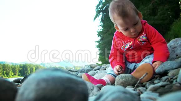 漂亮的小女孩正坐在一条河岸上玩石头视频的预览图