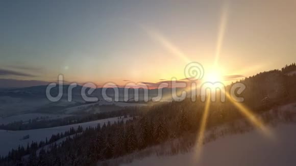 日出时飞越喀尔巴阡山雪山的鸟瞰图冬季的乡村景观视频的预览图