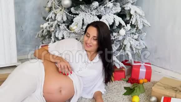带着圣诞礼物在圣诞树旁怀孕的妈妈视频的预览图