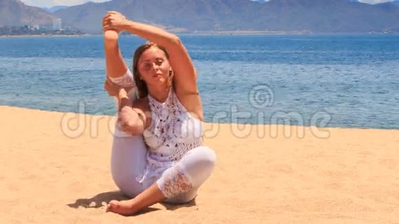 穿着白色蕾丝服装的女孩在沙滩上展示瑜伽体式腿视频的预览图