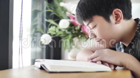 亚洲可爱的男孩一边看书一边等妈妈在咖啡馆买饮料视频的预览图