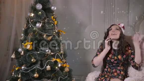 年轻可爱的英俊女孩在圣诞树附近用手机说话圣诞节庆典视频的预览图