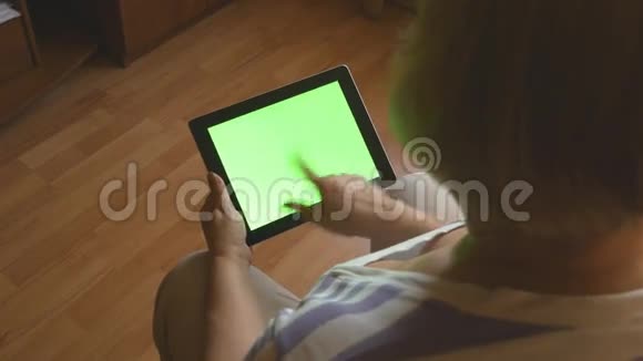 老年妇女坐在家里的沙发上使用带有绿色屏幕的数字平板电脑后视成人平板电脑视频的预览图