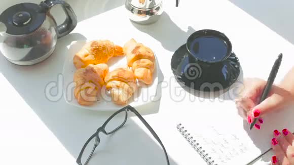 年轻漂亮的女孩在阳光明媚的日子里吃早餐在笔记本上写一封信视频的预览图