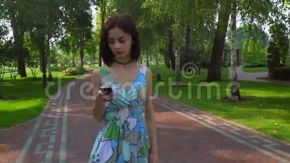 一个年轻的女孩在公园的一条小路上在电话里得到了一条信息视频的预览图