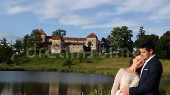 美丽浪漫的新婚夫妇新郎和新娘拥抱在日落的老城堡附近视频的预览图