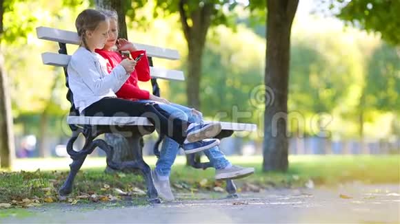 秋天带智能手机的可爱小女孩孩子们在温暖阳光的秋日户外玩耍视频的预览图