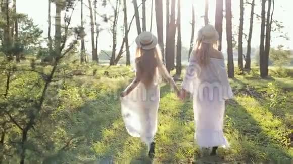 日落时分母亲和女儿穿着白色连衣裙戴着草帽在树林里玩耍视频的预览图