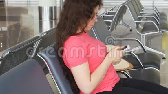 一位年轻的女士在机场等待出发看着智能手机视频的预览图