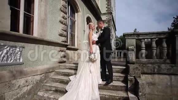 新郎和新娘站在楼梯上时尚模特穿着优雅的衣服白色长裙和时尚套装视频的预览图