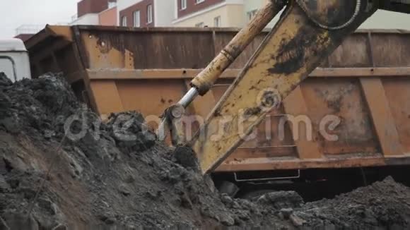 慢动挖掘机斗在建筑工地挖土并在卡车后面倾倒视频的预览图