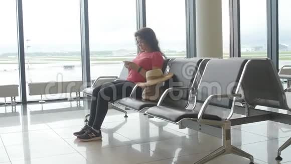一位年轻的女士在机场等待出发看着智能手机视频的预览图