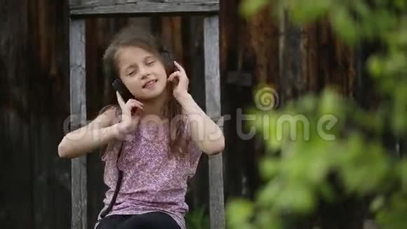 可爱的女孩坐在一个村庄的院子里喜欢带耳机的音乐视频的预览图