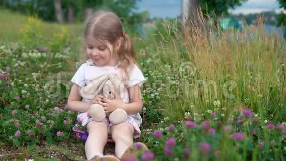 一个小女孩和一只玩具兔子在草地上的四叶草中玩耍视频的预览图