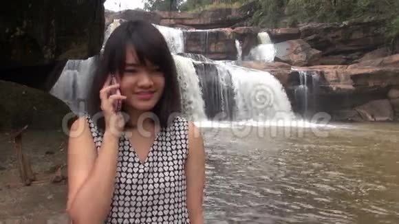 漂亮的女人在美丽的瀑布边用手机聊天视频的预览图