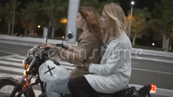 两个漂亮的年轻女人晚上骑摩托车在城市街道上互相交谈女司机和他女朋友视频的预览图